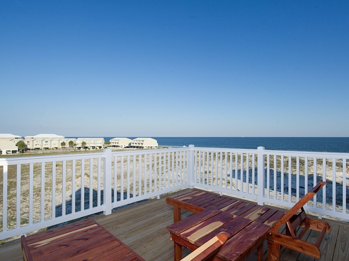 Una terraza de madera con barandilla blanca que da a una playa y al océano.