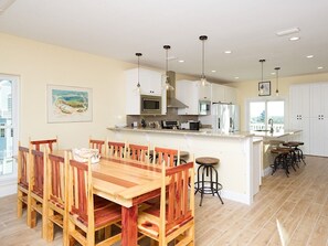 A spacious kitchen with wooden dining table and chairs, white cabinets, and pendant lighting.