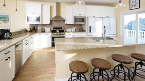 A modern kitchen with white cabinets, granite countertops, stainless steel appliances, and bar stools. - Grace | 6BR Fort Morgan Beach Retreat | Pet-Friendly | Gulf View (Gulf Shores)