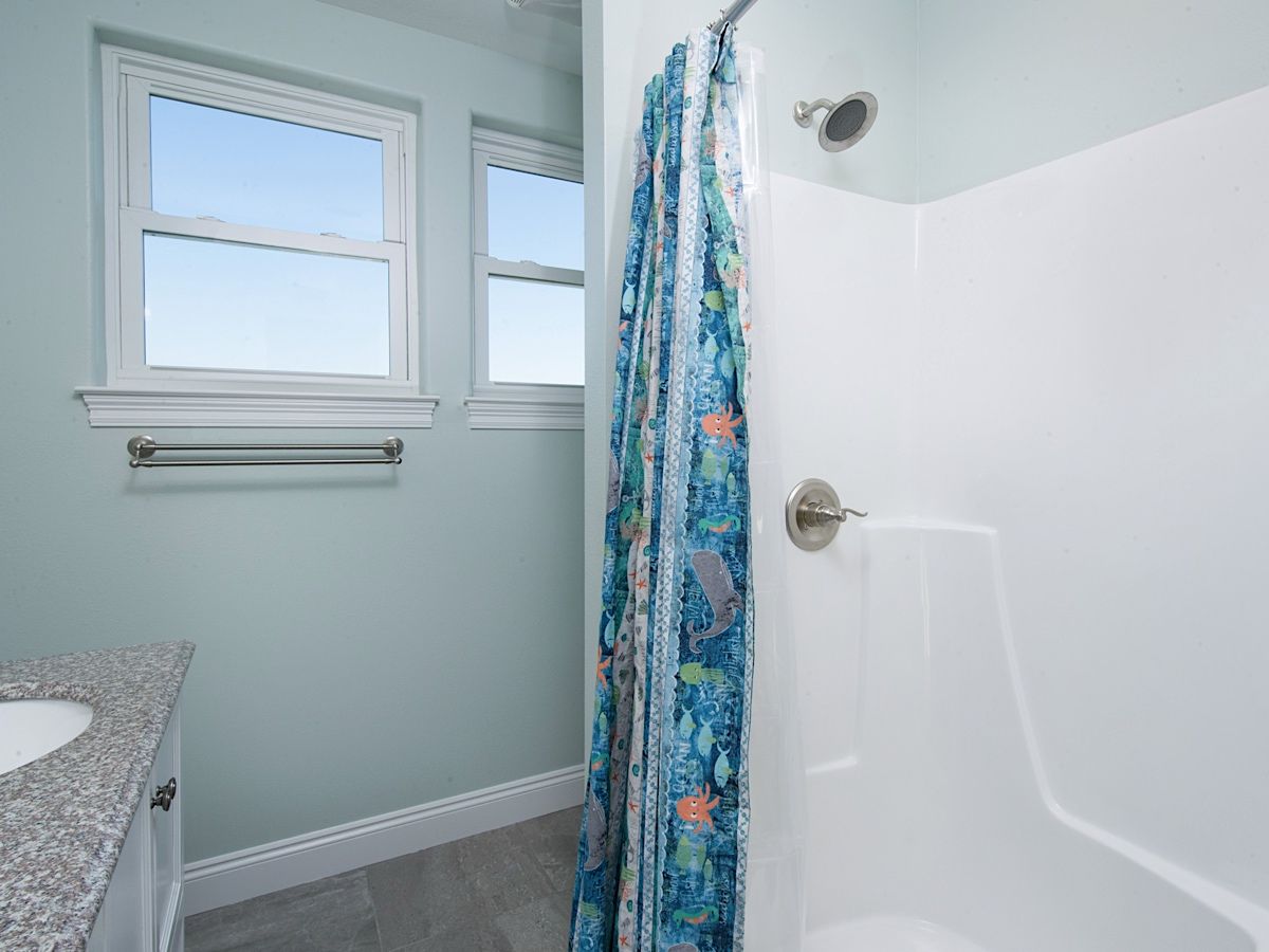 Une salle de bain avec une douche, un lavabo et deux fenêtres.