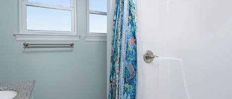 Une salle de bain avec une douche, un lavabo et deux fenêtres.