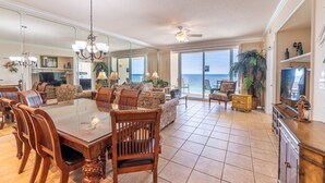 A spacious living area with a dining table, chairs, sofas, and a large window offering a view of the ocean. - Boardwalk 1111 4BR/3BA PCB Beachfront Luxury (Panama City Beach)