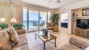 A spacious living room with a large glass door leading to a balcony, a ceiling fan, and a television on a wooden cabinet. - Boardwalk 1111 4BR/3BA PCB Beachfront Luxury (Panama City Beach)