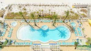 A large pool with palm trees, surrounded by lounge chairs and a sandy beach area. - Boardwalk 1111 4BR/3BA PCB Beachfront Luxury (Panama City Beach)