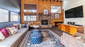 Ein gemütliches Wohnzimmer mit Kamin aus Stein, Holzwänden, einem großen Fernseher und bequemen Sitzmöglichkeiten.