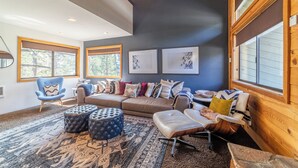 Ein modernes Wohnzimmer mit hohen Decken, großen Fenstern, einem braunen Sofa und einem blauen Sessel.