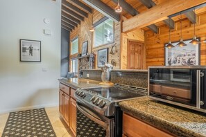 Une cuisine moderne dotée de plans de travail en granit, d’appareils électroménagers en acier inoxydable, de meubles de rangement en bois et d’un plafond orné d’un motif en chevrons.