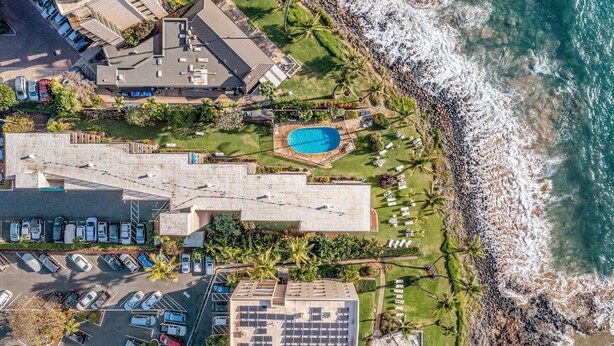 An aerial view of a coastal hotel with a swimming pool, parking area, and ocean view.