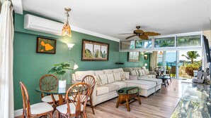 A spacious living room with a sofa, chairs, a glass coffee table, and a dining area with chairs and a table.