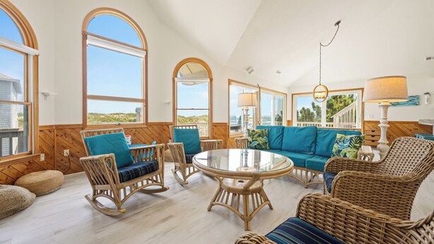 A spacious living area with wicker furniture, large windows, and a view of the outdoors. - Time To Coast: Semi-Oceanfront, Hot Tub, Ocean Views (Corolla)