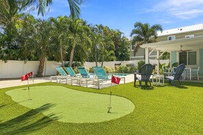 Zona de piscina con sillones de descanso y una piscina pequeña, rodeada de palmeras y una cerca blanca.