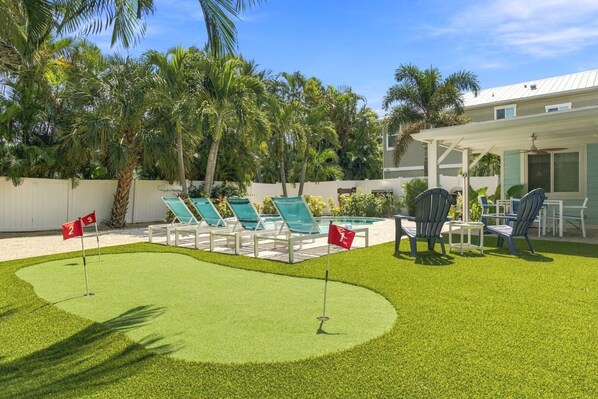 Área de piscina com espreguiçadeiras e uma piscina pequena, cercada por palmeiras e um muro branco.