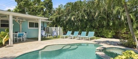 Una piscina con sillas de descanso y un porche cubierto.