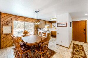 A dining area with a wooden table and chairs, a kitchen in the background, and a wooden door.