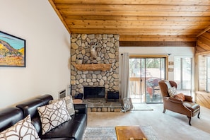 A living room with a stone fireplace, leather sofa, and a wooden ceiling.