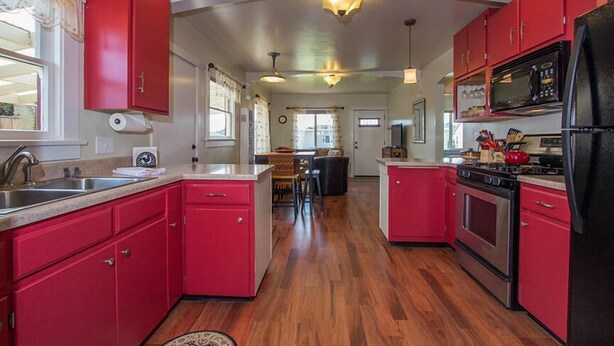 Una cocina con armarios rojos, electrodomésticos de acero inoxidable y piso de madera.