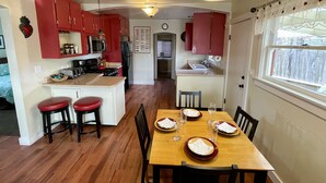 Cocina compacta con armarios rojos, una isla central con taburetes y una mesa de comedor preparada para cuatro.