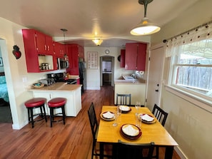 A compact kitchen with red cabinets, a central island with stools, and a dining table set for four. - Potter's Bungalow - Near Downtown Plaza, 3 bed (Arcata)