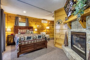 Un dormitorio rústico de cabaña con una cama grande, una chimenea y paredes de madera.