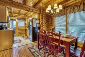 A wooden cabin interior with a dining area, kitchen, and a log wall.