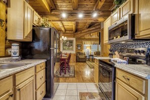 Une cuisine aménagée dans le style d’un chalet, avec des meubles de rangement en bois, un réfrigérateur, un four à micro-ondes et une cuisinière.