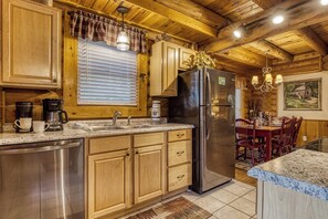 A wooden cabin kitchen with a stainless steel refrigerator, wooden cabinets, a coffee maker, and a dining area with a table and chairs. - Downtown Cabin w/Pool Table|Pool Access (PIGEON FORGE)