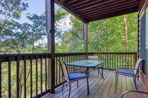 A covered outdoor deck with a table and chairs, surrounded by a wooden railing and lush greenery. - Downtown Cabin w/Pool Table|Pool Access (PIGEON FORGE)