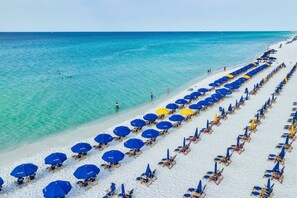 A beach with rows of sun loungers and umbrellas, a clear blue sea, and a white sandy shore.
