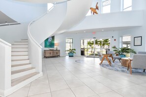 A spacious lobby with a curved staircase, a seating area with chairs and a table, and a large window offering a view of the outdoors.