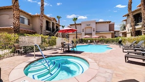 A pool area with lounge chairs, a hot tub, and a sign indicating pool capacity and lifeguard duty hours.
