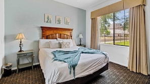 A hotel room with a large bed, two bedside tables, a window with curtains, and wall art.