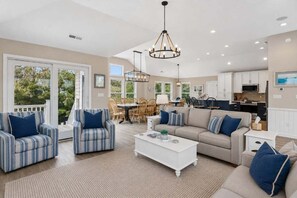 A spacious living area with a sofa, armchairs, and a coffee table. There is a dining area with chairs and a table. The kitchen is visible with cabinets and appliances. - OCEANSIDE:  Elegant home! Private Pool, Hot Tub, Gameroom with Pool Table! (Corolla)