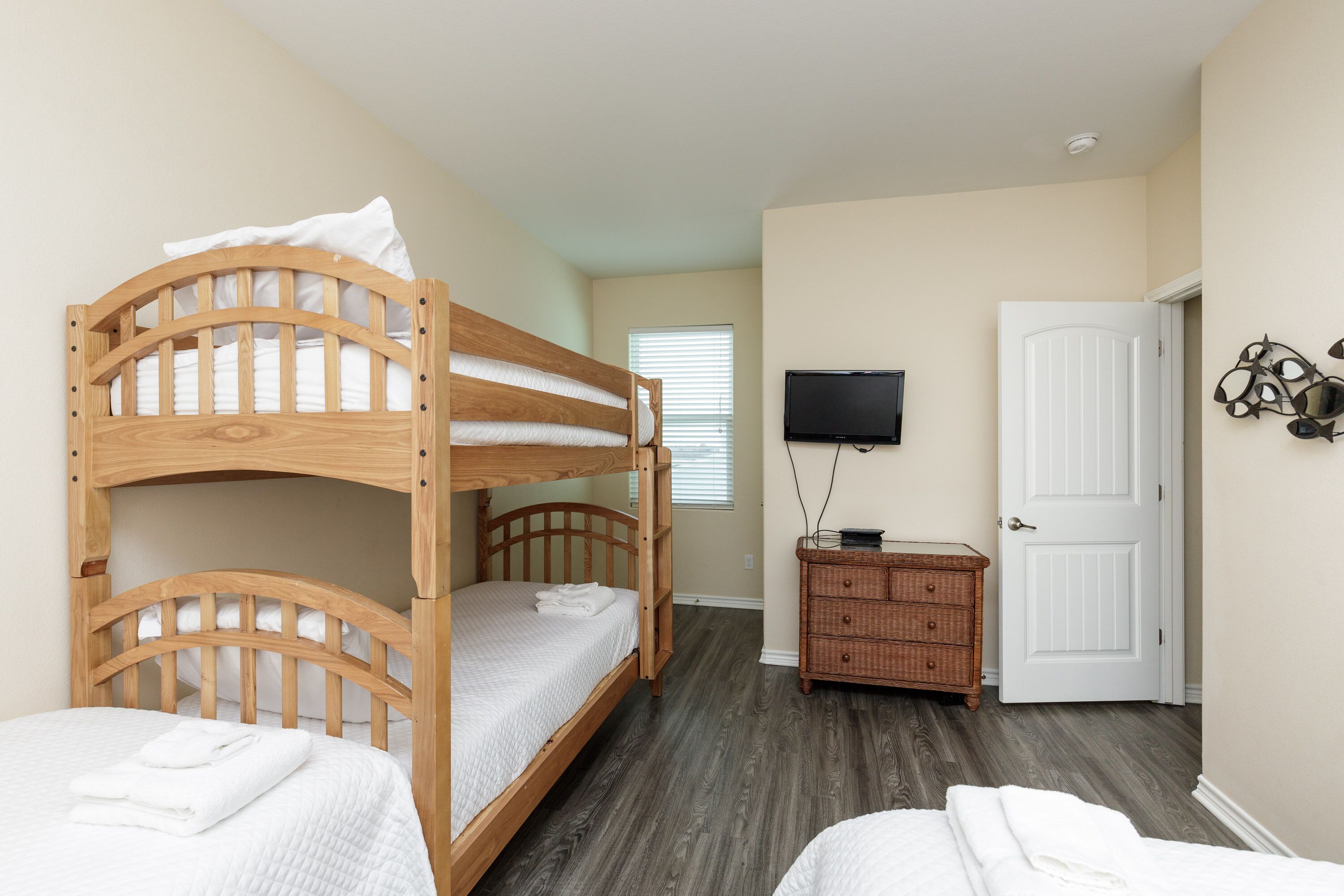 A bedroom with a bunk bed, a dresser, a television, and a door.