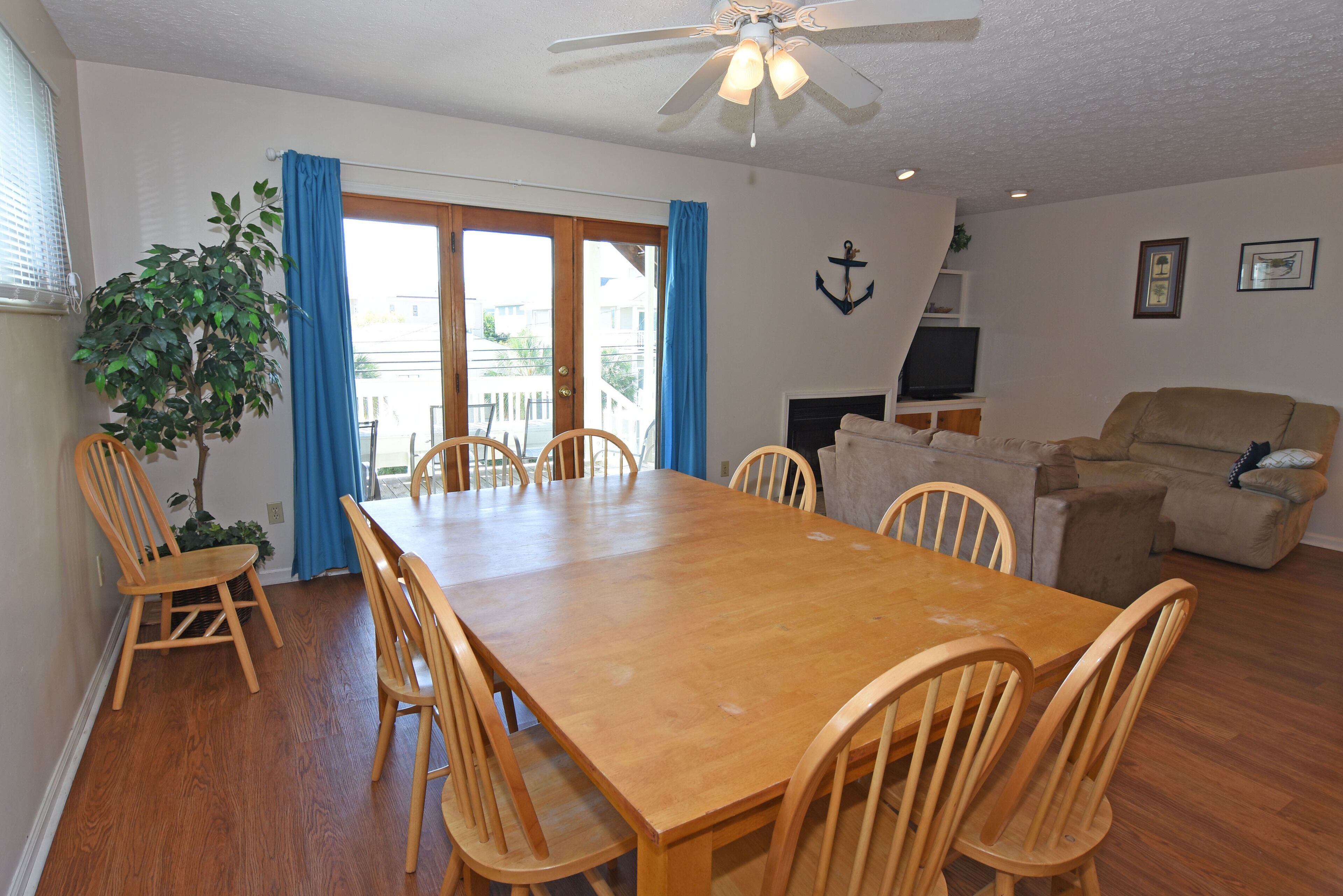 A dining area with a wooden table and chairs, a ceiling fan, and a view through a glass door.