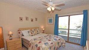Un dormitorio con cama, mesitas de noche, ventilador de techo y vistas a un balcón.