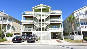 Un edificio residencial de varios pisos con balcones, un vestíbulo cubierto y un aparcamiento con dos coches.