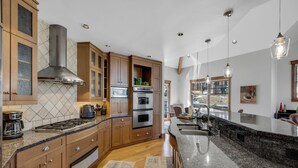 A spacious kitchen with wooden cabinets, a stainless steel range hood, granite countertops, and a large island with a sink. - Exquisite Spacious Breck Chalet. Walk to Slopes. Gourmet Kitchen. Large Deck (Breckenridge)