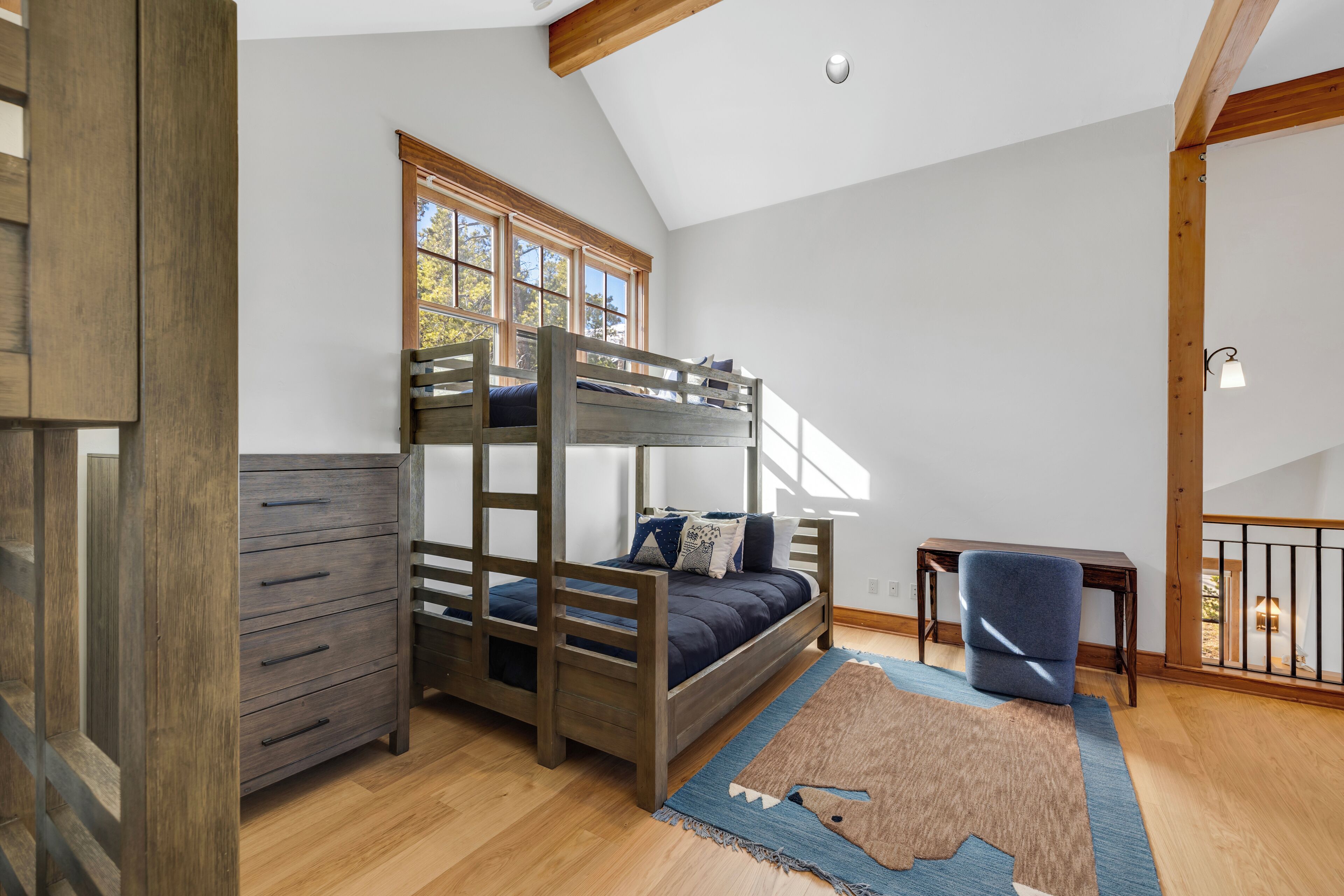 Un lit superposé avec une commode, une chaise et un tapis dans une pièce au plancher en bois et au plafond en pente.