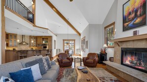 A spacious living room with a fireplace, leather chairs, a sofa, and a dining area with a kitchen in the background. - Exquisite Spacious Breck Chalet. Walk to Slopes. Gourmet Kitchen. Large Deck (Breckenridge)