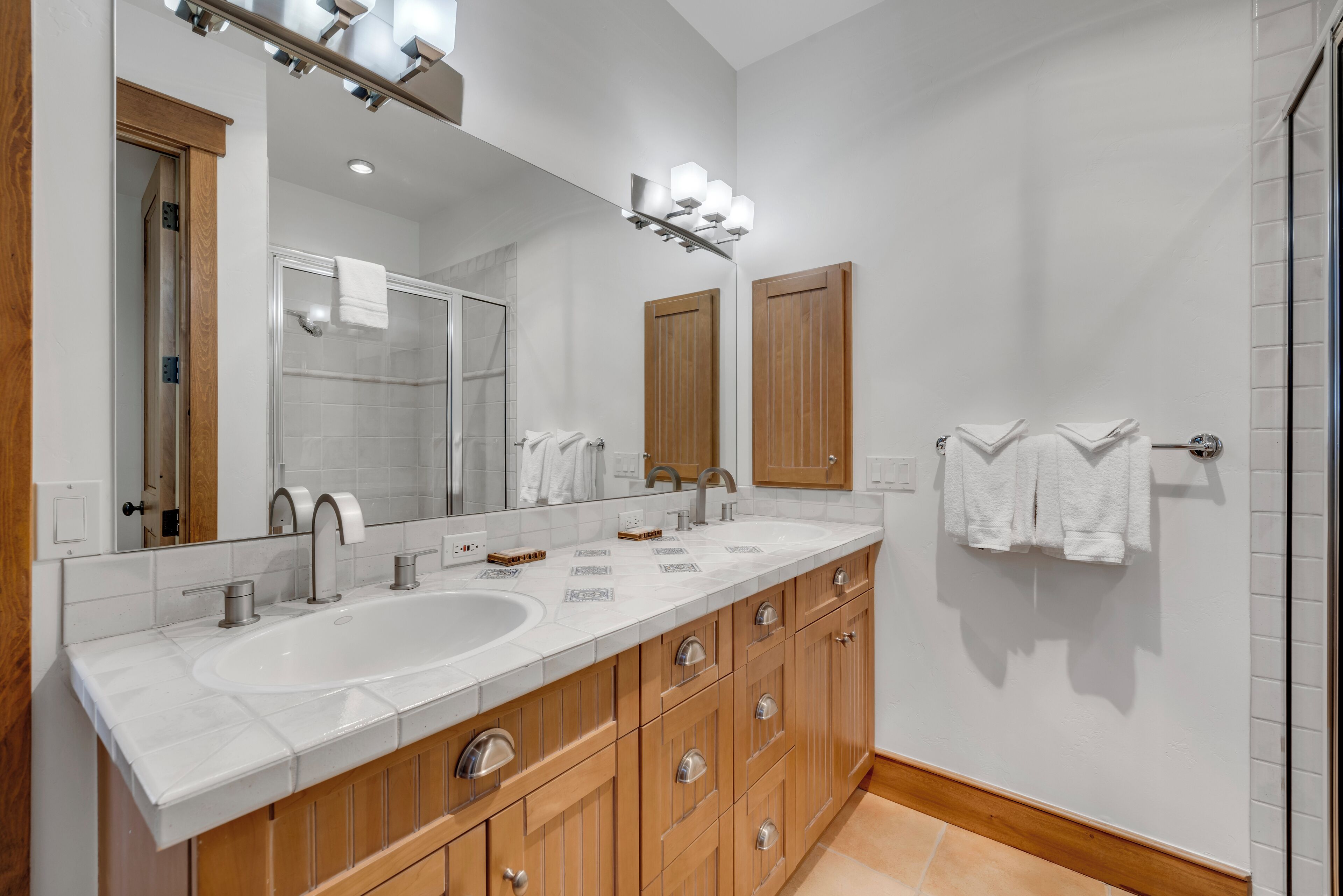 Une salle de bain moderne avec un grand miroir, deux vasques, des meubles en bois et un espace douche.