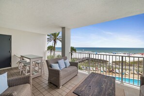 Un balcone con vista sulla spiaggia, un divano in vimini, un tavolino e una panca in legno.