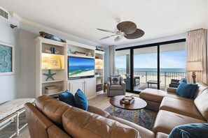 A living room with a TV, leather sofa, and a balcony with a view of the ocean.