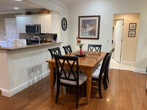 Un coin repas avec une table et des chaises en bois, une cuisine à l’arrière-plan et un tableau encadré au mur.