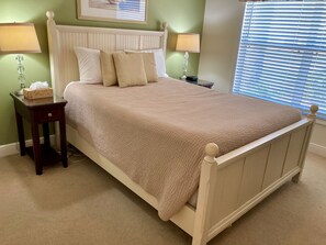 A bed with a white headboard, two bedside tables with lamps, and a window with blinds.
