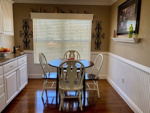 A dining area with a round table, four chairs, and a window with blinds.