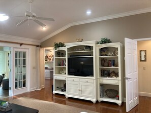 A spacious living room with a white entertainment center, a ceiling fan, and a door leading to another room.