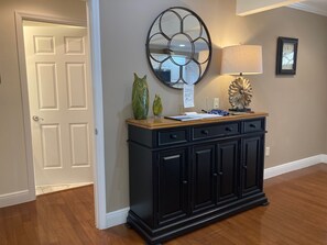 A hallway with a black cabinet, a mirror, a sign, and a lamp.