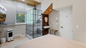 Une chambre moderne avec un grand lit, une douche en verre, un escalier en bois et une vue sur les arbres par la fenêtre.