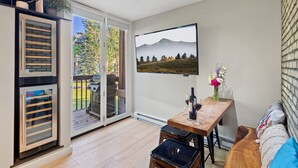 Un salon moderne avec une table en bois, un canapé et un téléviseur fixé au mur, qui diffuse une image d’un paysage de montagne.