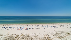 Een strand met vele parasols en ligstoelen, een zandstrand en de oceaan.